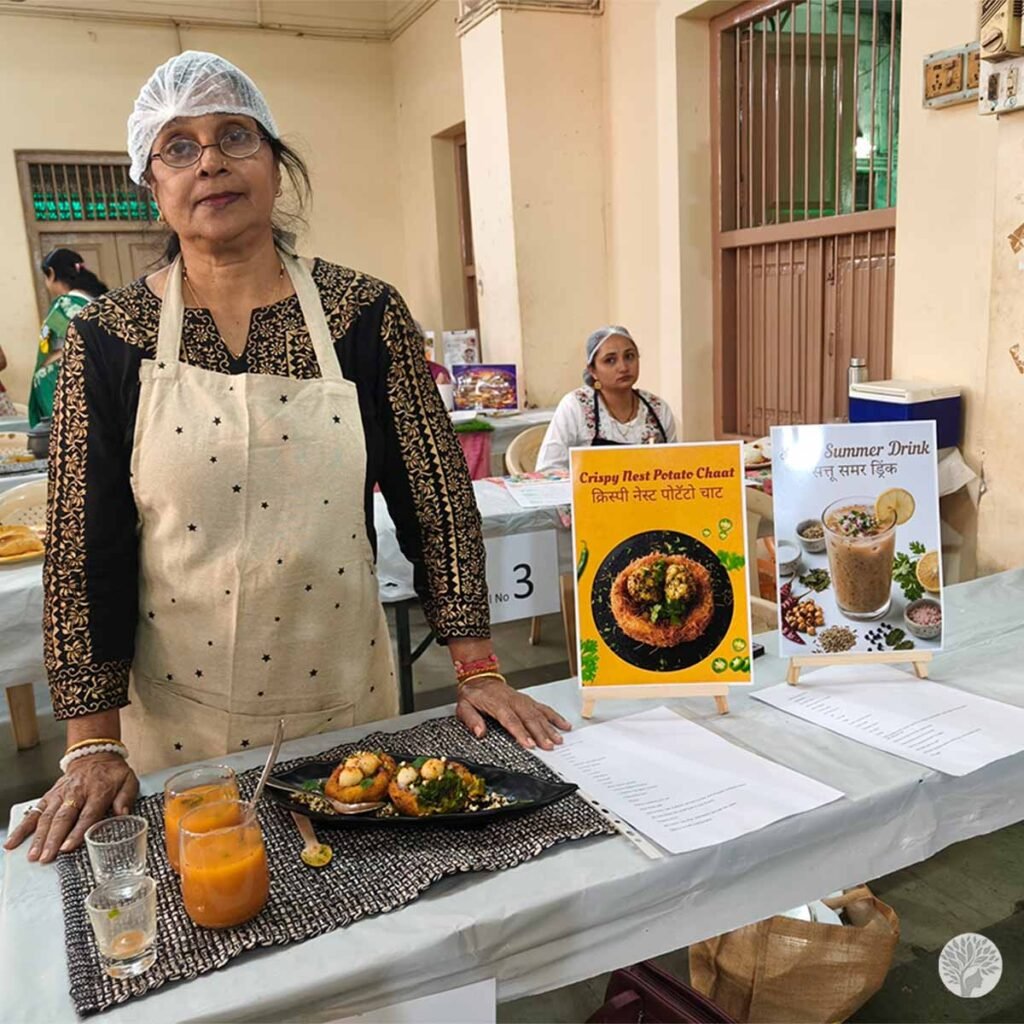 A participant at stall number one demonstrating a calm cooking routine next to her Crispy Nest Potato Chaat and Sattu Summer Drink at a Baroda cooking contest.