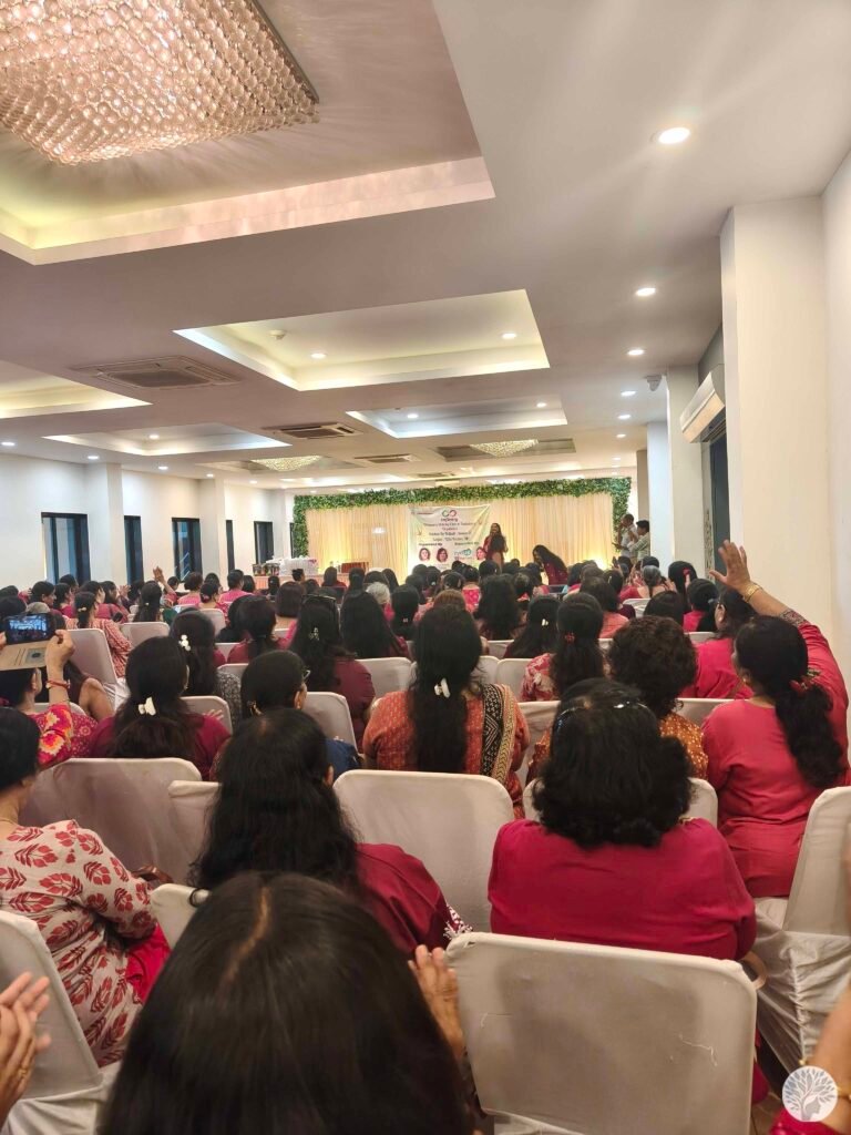 A large audience of women wearing shades of red and pink seated in a banquet hall, watching a health awareness seminar and stage presentation at the Kitchen Ke Khiladi event.