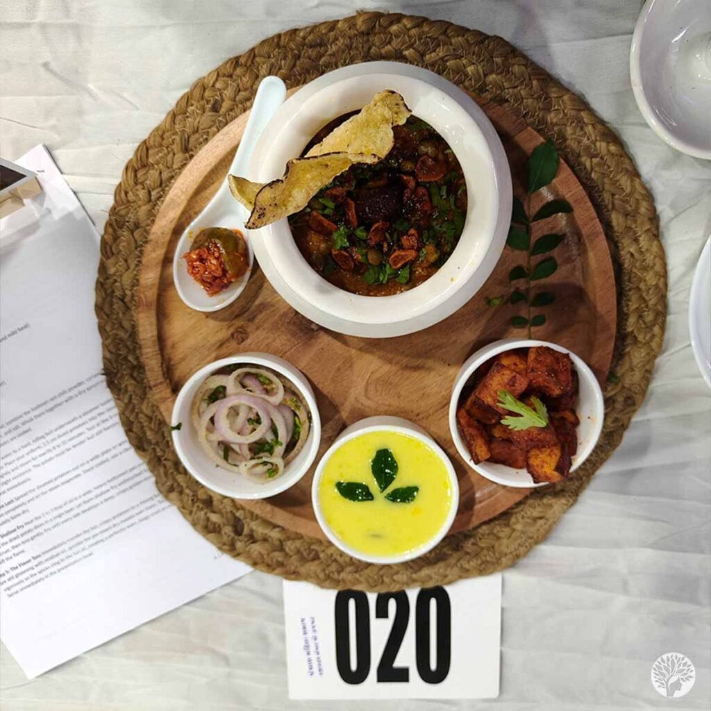 Overhead top-down view of a traditional Kathiyawadi platter with Girnari Tuvar Ringan Khichadi, yellow yogurt kadhi soup, and crispy potato fry on a wooden tray.