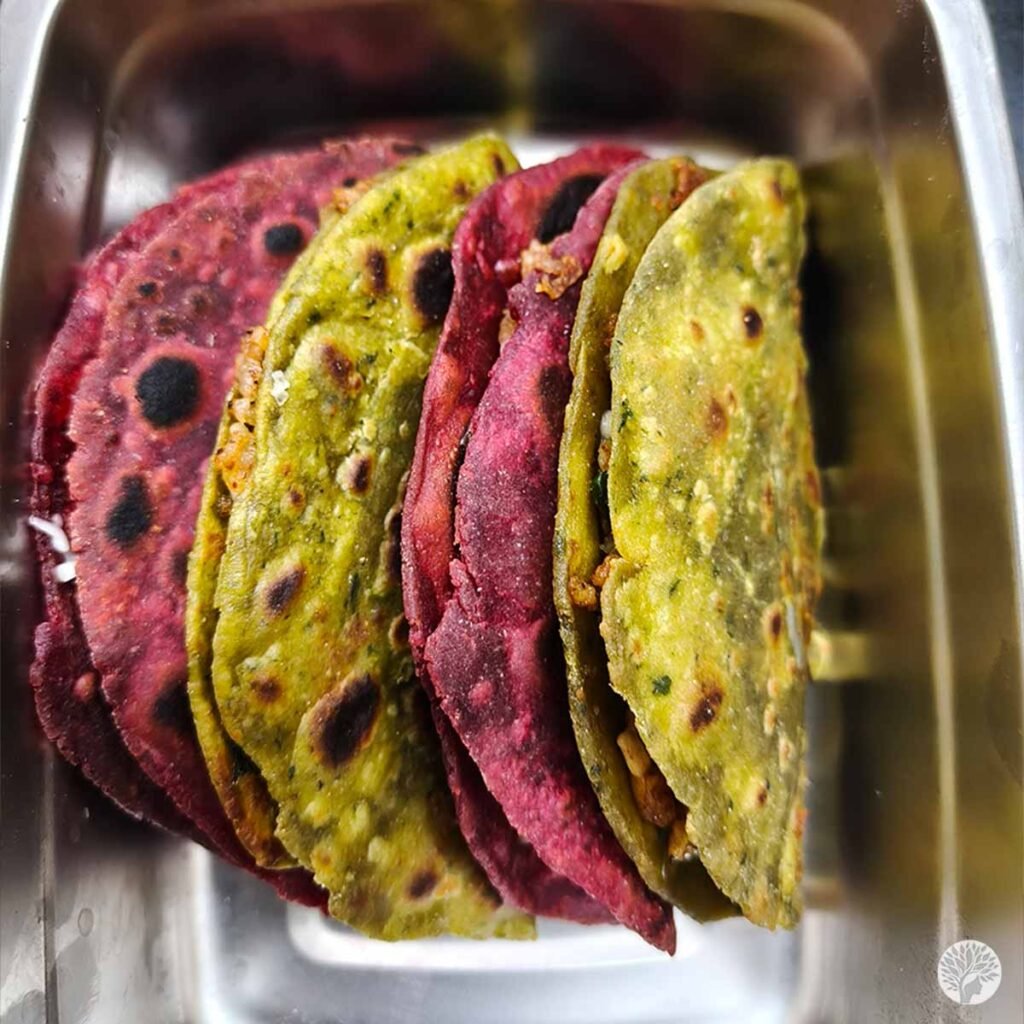 Soft, colorful homemade whole wheat tacos with alternating green and deep pink shells packed tightly inside a stainless steel school tiffin lunch box.